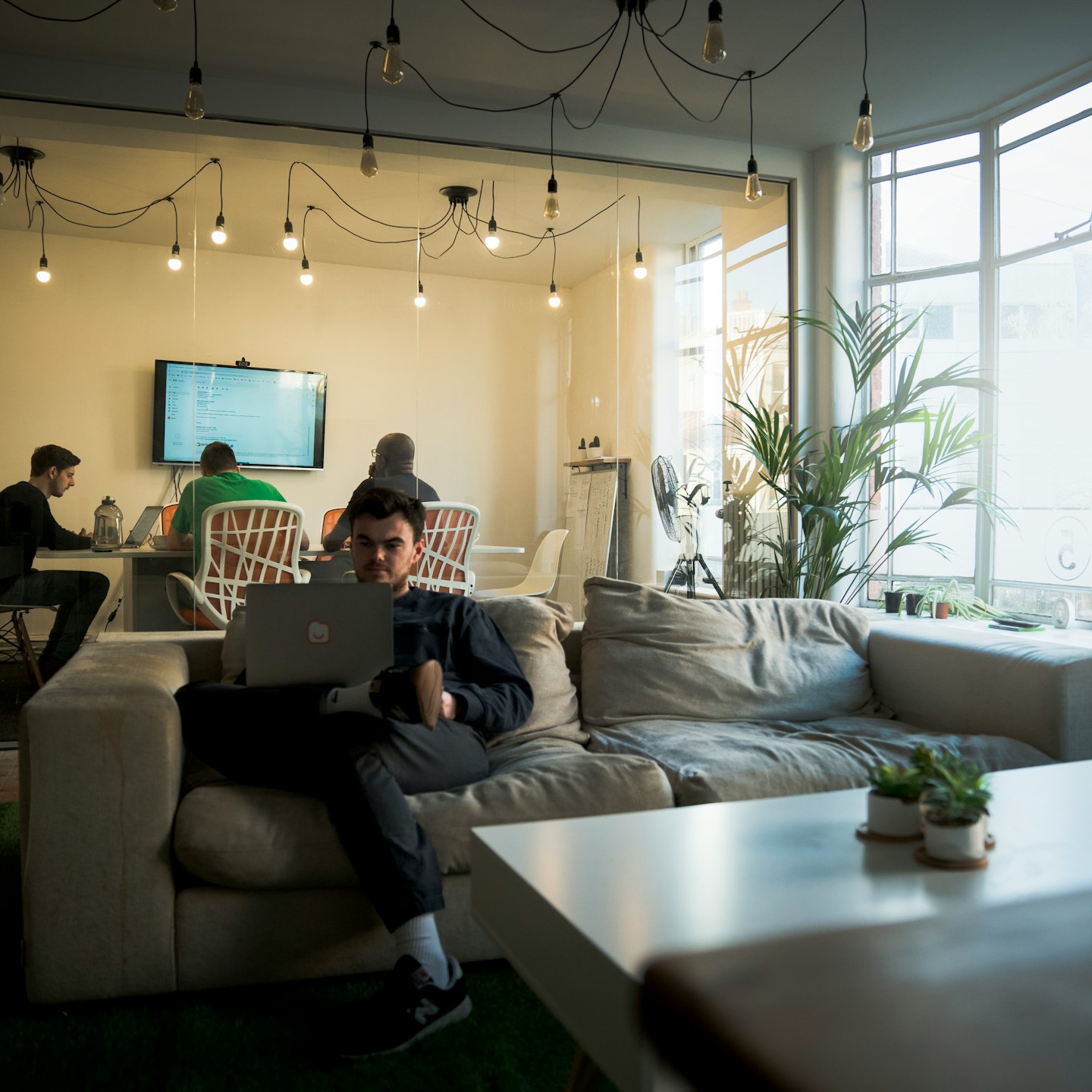 A man works on his laptop while seated on a sofa.
